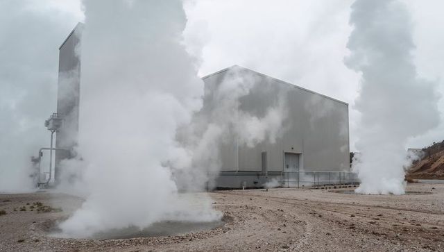 Geothermal facility emitting dense steam plumes around corrugated metal industrial site