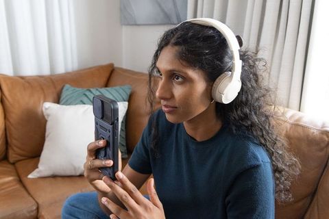 Young woman sitting on leather sofa listening with white headphones holding smartphone