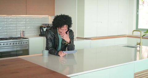 African american man laughing while using tablet on minimalist kitchen island with mug