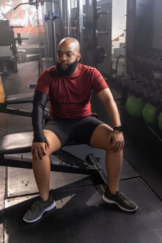 Bearded man sitting on bench checking smartwatch in gym resting between sets