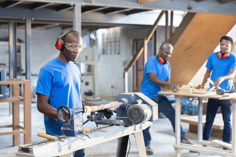 African american woodworkers collaborating on lathe turning and sanding in workshop