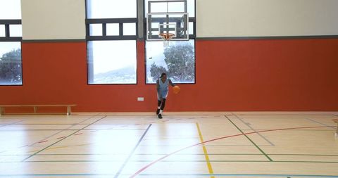 Teenage Male Athlete Dribbling Basketball in Gymnasium