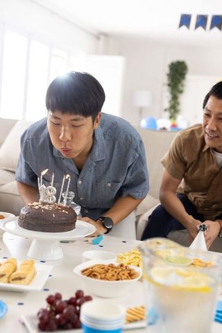 Young man blowing out 18th birthday candles at home party with family and snacks