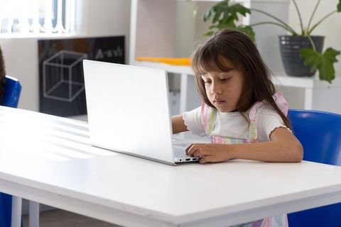 Schoolgirl typing on laptop in sunlit classroom focused on digital learning and study