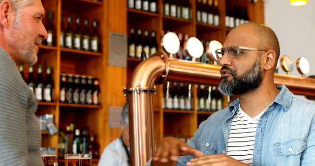 Bartender wearing glasses and customer engaging in conversation in a welcoming pub. Wooden shelves filled with bottles create a warm atmosphere. Perfect for illustrating hospitality, social interactions, community, relaxed environment, or pub culture.