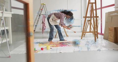 Contemporary artist painting on floor canvas in bright studio holding palette and brush