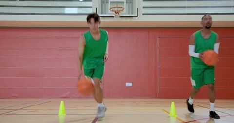 Diverse male players dribbling through cones during basketball agility drill