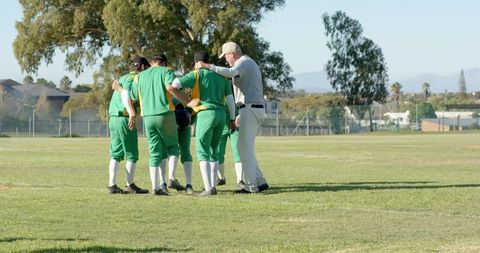 Baseball team huddling with coach on sunlit suburban field showing teamwork and camaraderie
