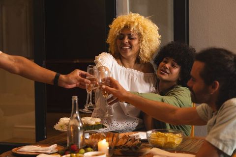 Diverse friends toasting with wine around cozy candlelit dinner table at home gathering