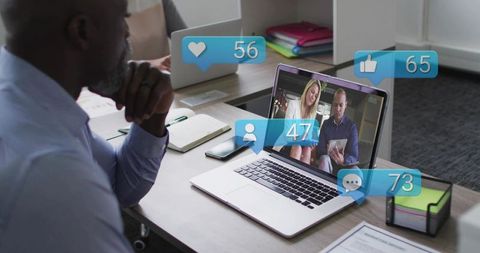 Mature professional watching virtual meeting on laptop with social engagement overlays