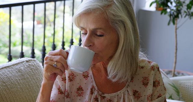 A senior Caucasian woman enjoys a cup of coffee in a cozy home environment, with copy space. Her relaxed demeanor suggests a moment of tranquility during her daily routine.