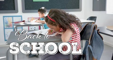 Focused elementary girl writing at desk wearing red headband striped top back to school
