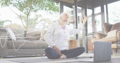 Senior woman practicing gentle yoga at home with tablet in bright minimal living room
