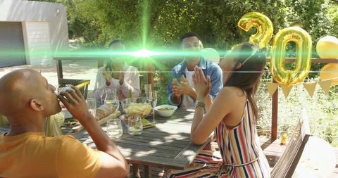 Friends celebrating 30th birthday on sunlit backyard deck with gold balloons and snacks
