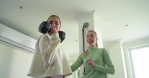 Female fitness coach spotting dumbbell curl at home while smiling and encouraging