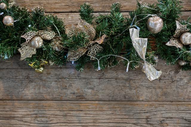 Christmas garland adorned with gold ornaments and ribbons on rustic wooden background. Ideal for holiday greeting cards, festive invitations, seasonal blog posts, and Christmas-themed advertisements.