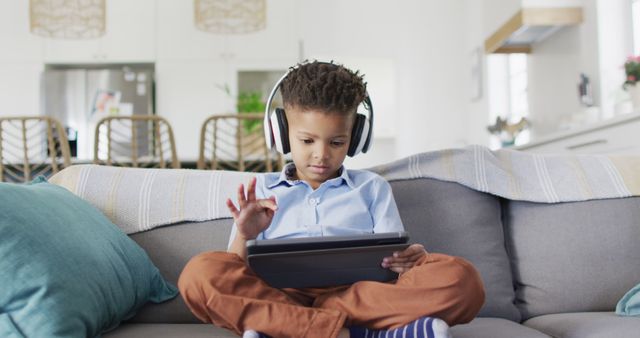 Happy african american boy sitting on sofa and using tablet. Spending quality time at home, childhood and technology concept.