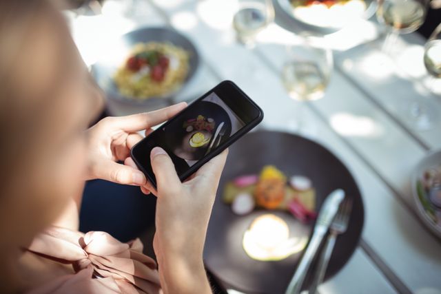 Woman capturing a photo of a gourmet meal with her smartphone in a restaurant. Ideal for use in articles or advertisements related to food photography, social media trends, dining experiences, and lifestyle blogs.