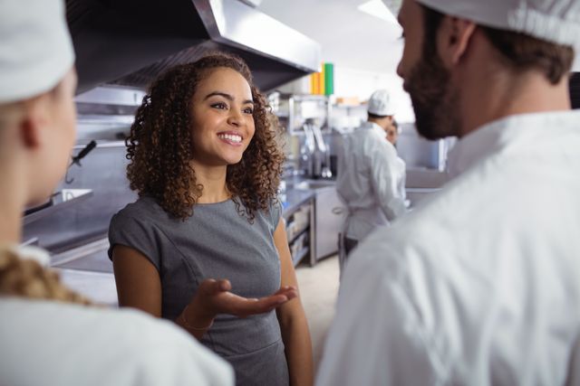 Restaurant manager engaging with kitchen staff in commercial kitchen. Image depicts teamwork and professional interaction in hospitality industry. Useful for training materials, business presentations, culinary school promotions, and articles about effective management and team collaboration in restaurants.