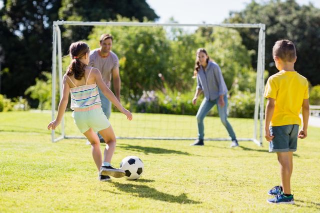 Family enjoying a sunny day at the park, playing football together. Children and parents engaging in a fun outdoor activity, promoting bonding and teamwork. Ideal for use in advertisements, family-oriented content, and recreational activity promotions.