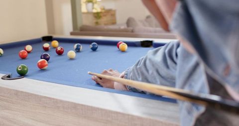Man lining up precise shot on blue-felt pool table in cozy contemporary home lounge