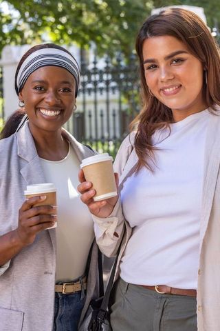 Smiling african american friends holding takeaway coffee cups outdoors in sunny urban park