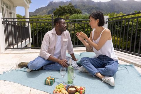 Couple enjoying romantic terrace picnic sharing wine and fruit platter with mountains