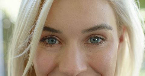 Sunlit closeup portrait of smiling blonde woman showing blue-green eyes and skin texture