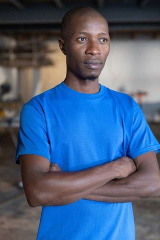 Confident african american craftsman standing arms crossed in industrial workshop