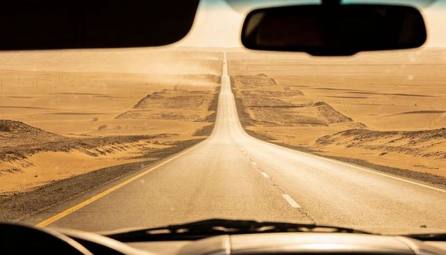 Driving along endless sunlit desert highway from windshield view with dashboard and wheel