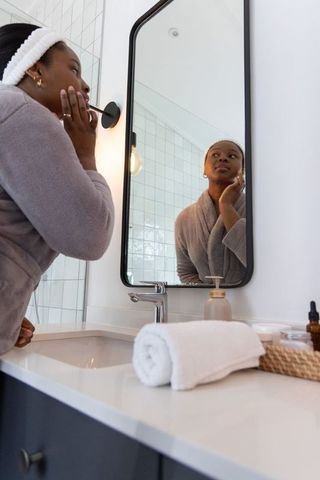 African american woman applying skincare at vanity mirror in modern minimal bathroom