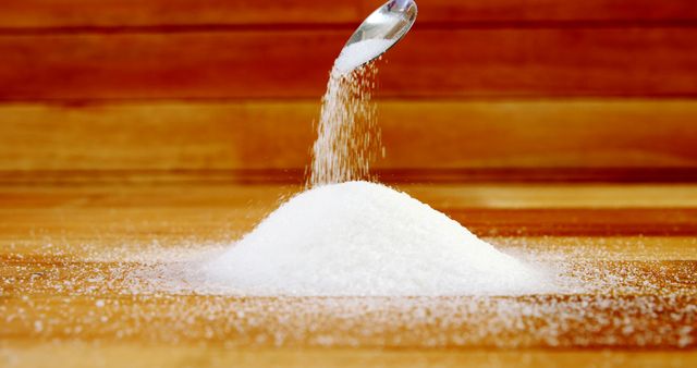 Sugar is being poured onto a wooden surface, creating a small mound, with copy space. Its granules glisten as they catch the light, emphasizing the texture and motion of the pour.