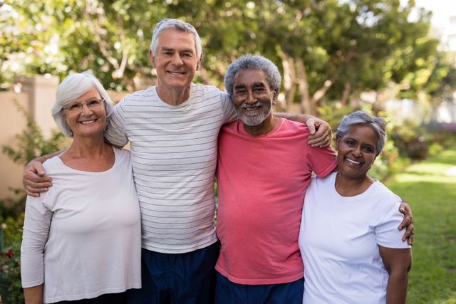 Group of senior friends standing together in a park, smiling and embracing each other. Ideal for use in advertisements, brochures, and articles related to senior living, friendship, active lifestyle, and community engagement.