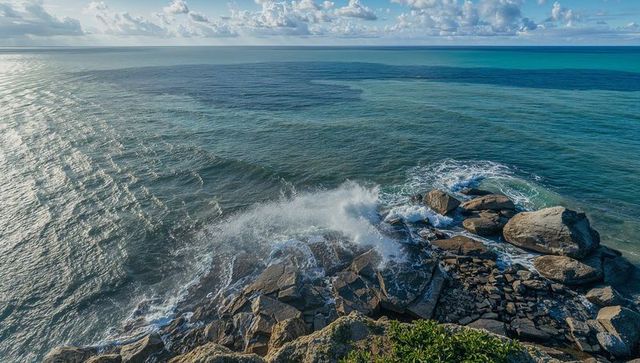 Waves crashing against rocky headland with turquoise ocean, foam spray and dramatic sky