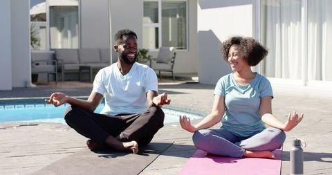 Couple meditating by pool on yoga mats smiling practicing outdoor wellness and harmony