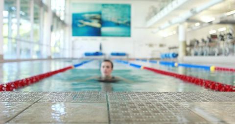 Female athlete treading water facing camera in indoor lap pool with red lane ropes