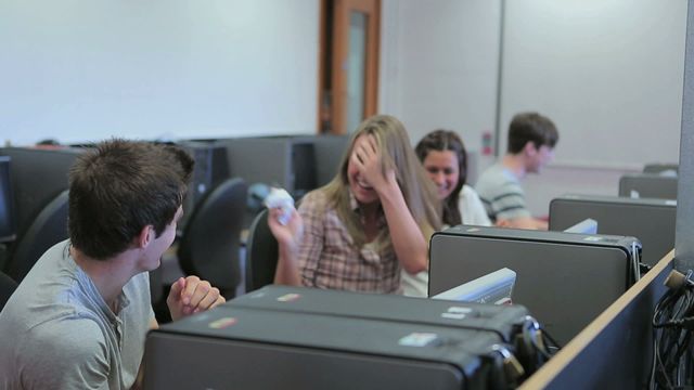 Students having fun with paper airplanes in a computer lab setting, showing a casual and relaxed atmosphere. Ideal for use in educational content, youthful lifestyle promotions, or educational technology advertisements. Can be used to illustrate the informal side of learning environments or engage a younger audience.