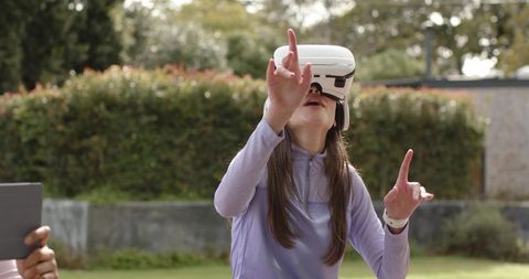Adult woman wearing vr headset reaching and interacting with virtual elements outdoors