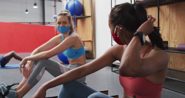 Two diverse women wearing face masks talking at the gym. two women working out on rowing machines taking a break and chatting. hygiene at gym during coronavirus covid 19 pandemic
