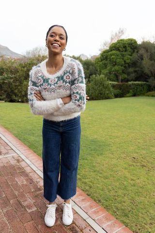 Smiling african american woman wearing fuzzy sweater standing on garden walkway