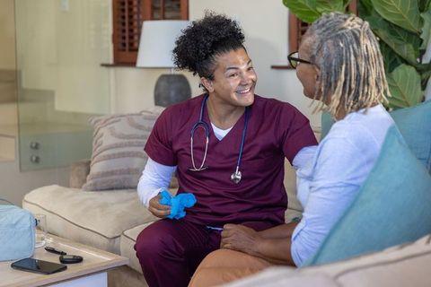 Home nurse visiting senior african american woman smiling and holding hand