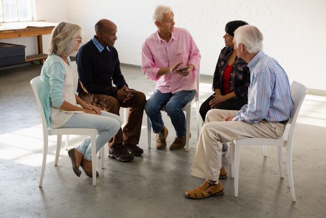 Senior friends are sitting in a circle, engaging in a lively group discussion in an art class. This image can be used for promoting community activities, senior education programs, social clubs, and active retirement lifestyles. It highlights the importance of social interaction and lifelong learning among elderly individuals.