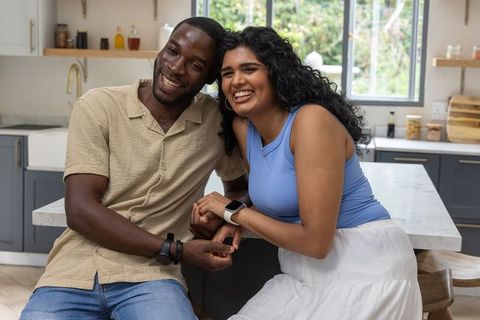 Indian woman and african american man sharing warm laugh at modern marble kitchen island