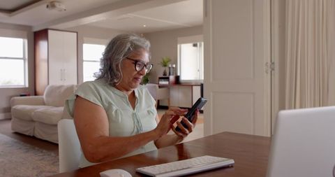 Elderly Woman Celebrating Achievement Using Smartphone in Home Office