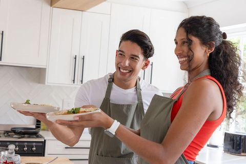 African american couple serving homemade meals in sunlit modern kitchen, smiling duo
