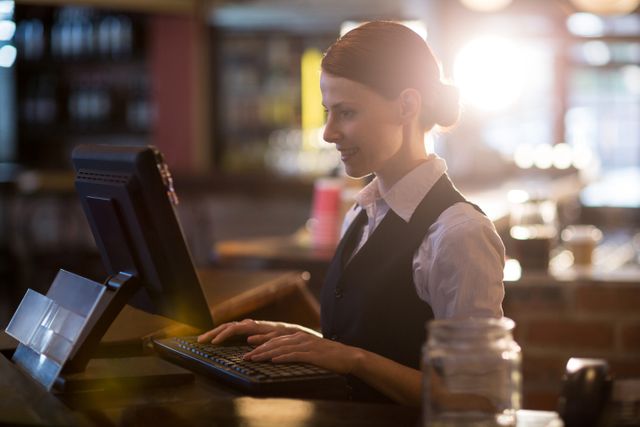 Waitress in uniform using a computer at a restaurant counter. Ideal for illustrating themes related to hospitality, customer service, restaurant management, and modern technology in the food service industry. Can be used in articles, blogs, and marketing materials for restaurants, cafes, and bars.