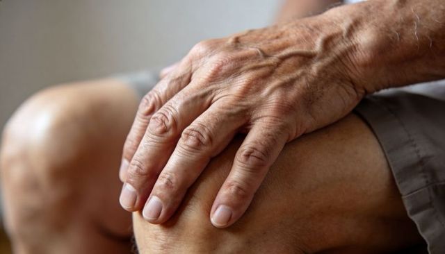 Elderly man resting hand on knee close-up showing veins wrinkles skin texture aging hands