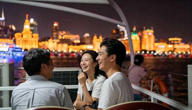 Laughing friends enjoying night ferry cruise with illuminated city skyline and river reflections