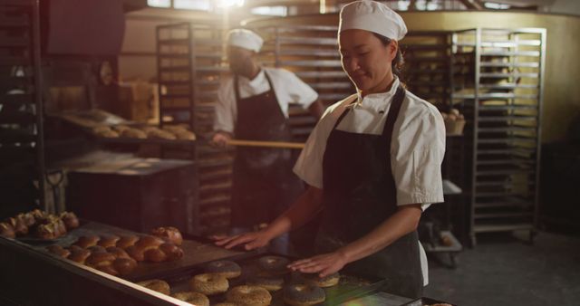 Image of happy asian female baker arranging croissants on tray. working at bakery, independent small business.