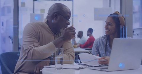 Senior professional advising young colleague during collaborative office meeting with laptop